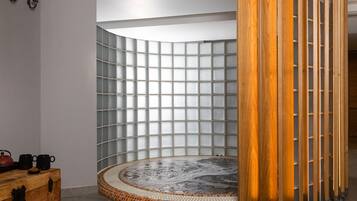 A modern bathroom with a glass-enclosed shower, a wooden bench, and a tiled floor.