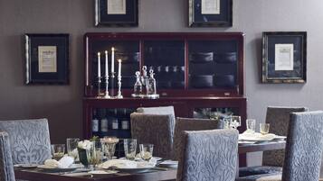 A dining room with a dark wooden cabinet, framed certificates on the wall, and a table set for four with chairs.