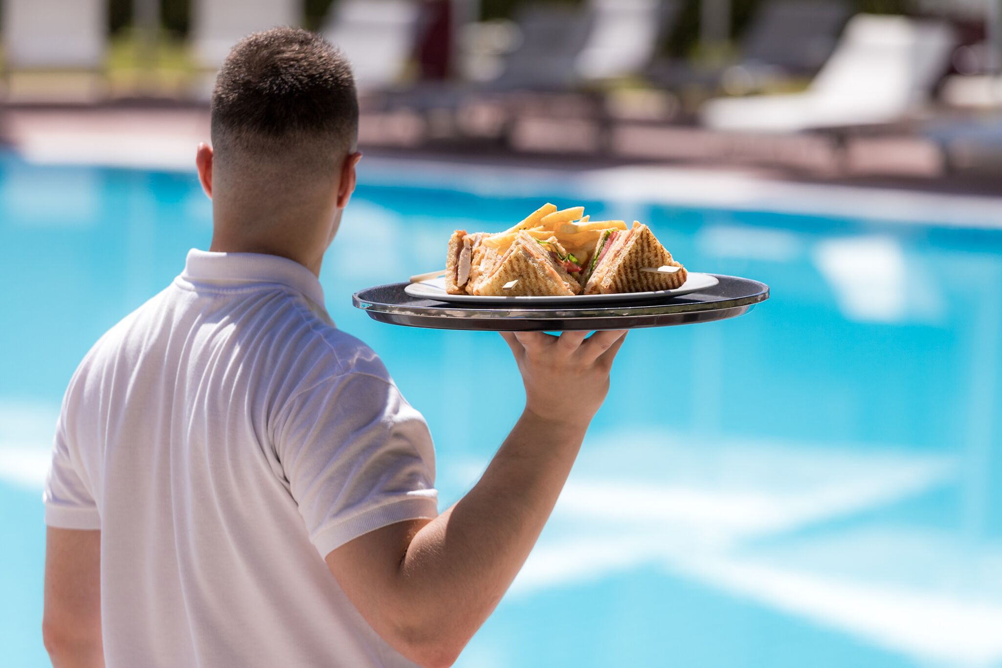 Una persona sosteniendo una bandeja con sándwiches junto a una piscina.