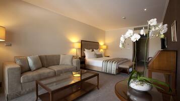 A hotel room with a bed, a sofa, a coffee table, and a dining table with a flower vase.
