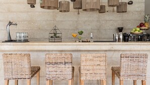 Una cocina con sillas de mimbre, encimera de mármol, lámparas colgantes de mimbre y una exposición de frutas.