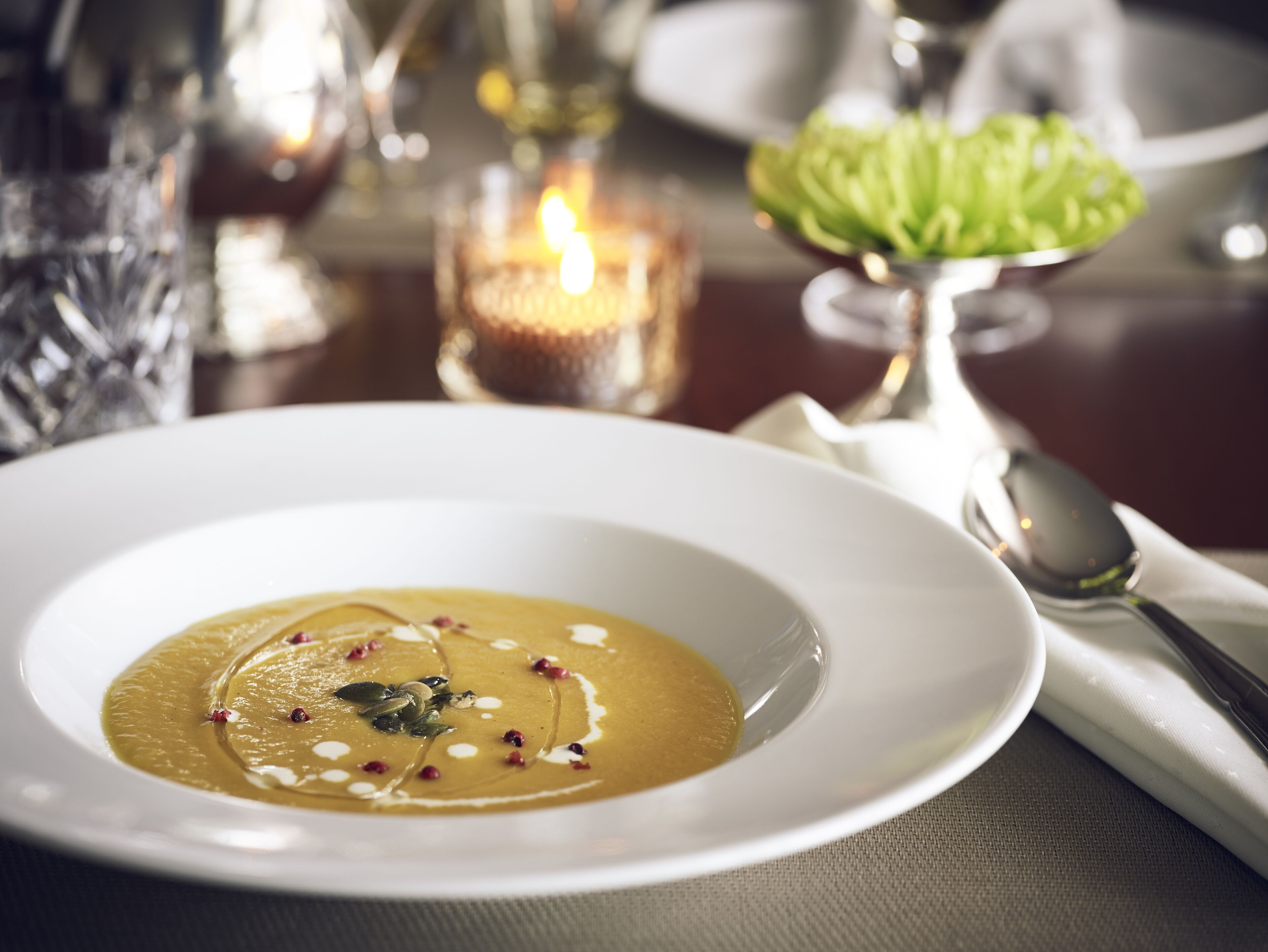 A white plate with a creamy soup garnished with seeds and a candle in the background.
