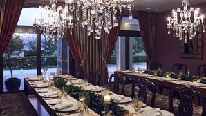Un comedor formal con una larga mesa dispuesta para una comida, candelabros elegantes y vistas a un jardín paisajístico a través de amplias ventanas.
