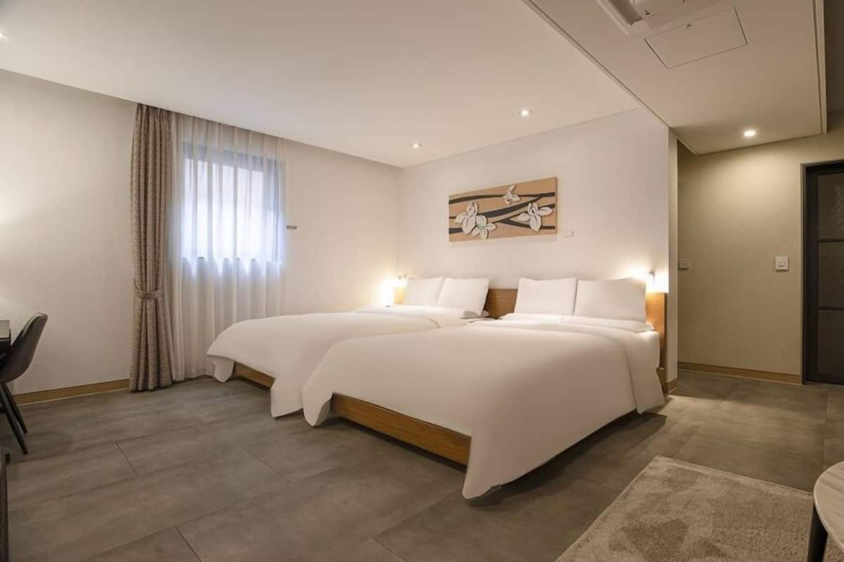 A hotel room with two beds, a dining area, and a large window with curtains.