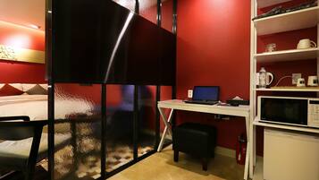 Une chambre d’hôtel compacte comprenant un lit, un bureau avec un ordinateur portable, un four à micro-ondes et un petit réfrigérateur.