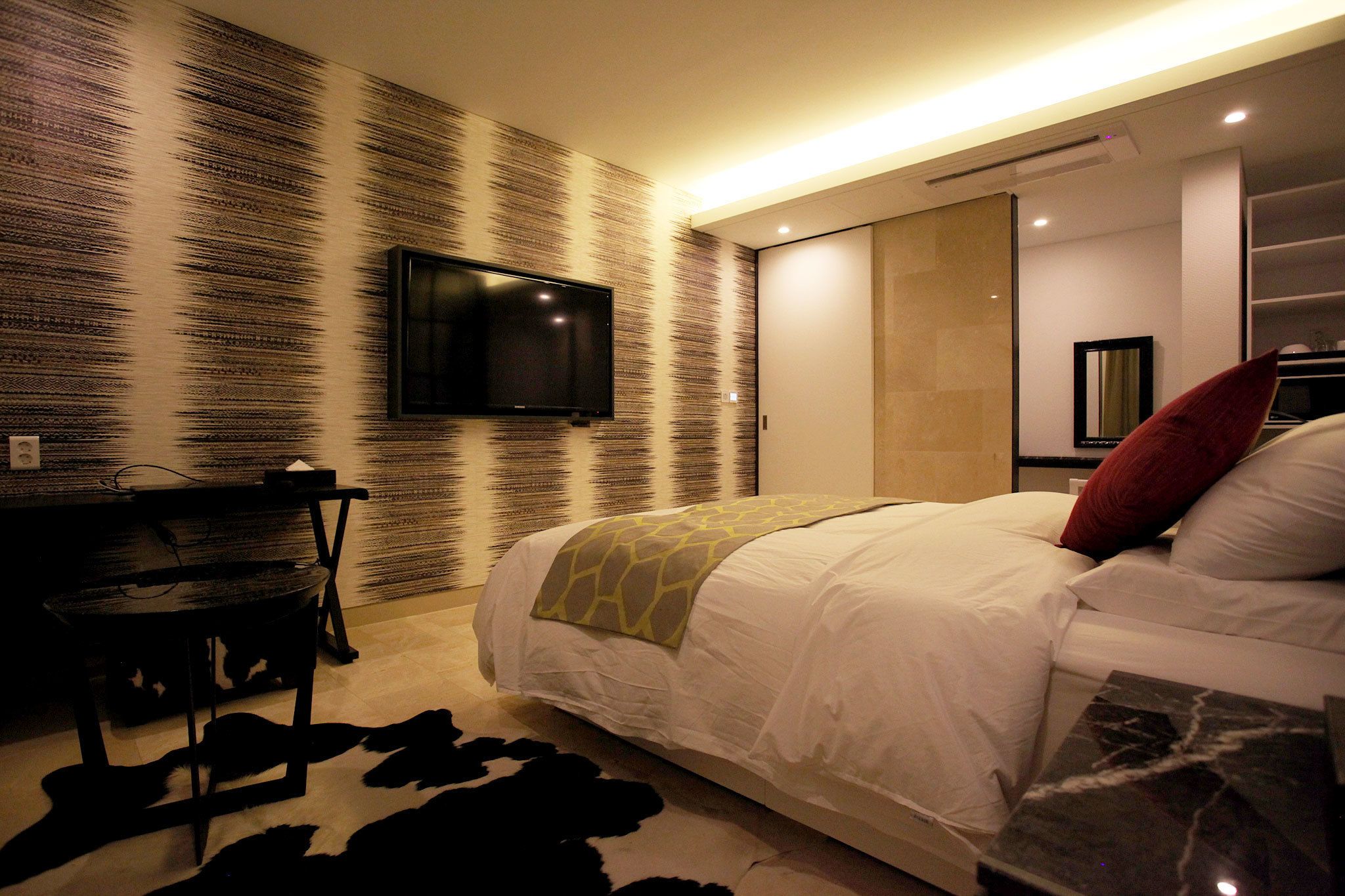 Un dormitorio moderno con una cama grande, un televisor de pantalla plana montado en la pared, una mesita pequeña y un original diseño de pared.