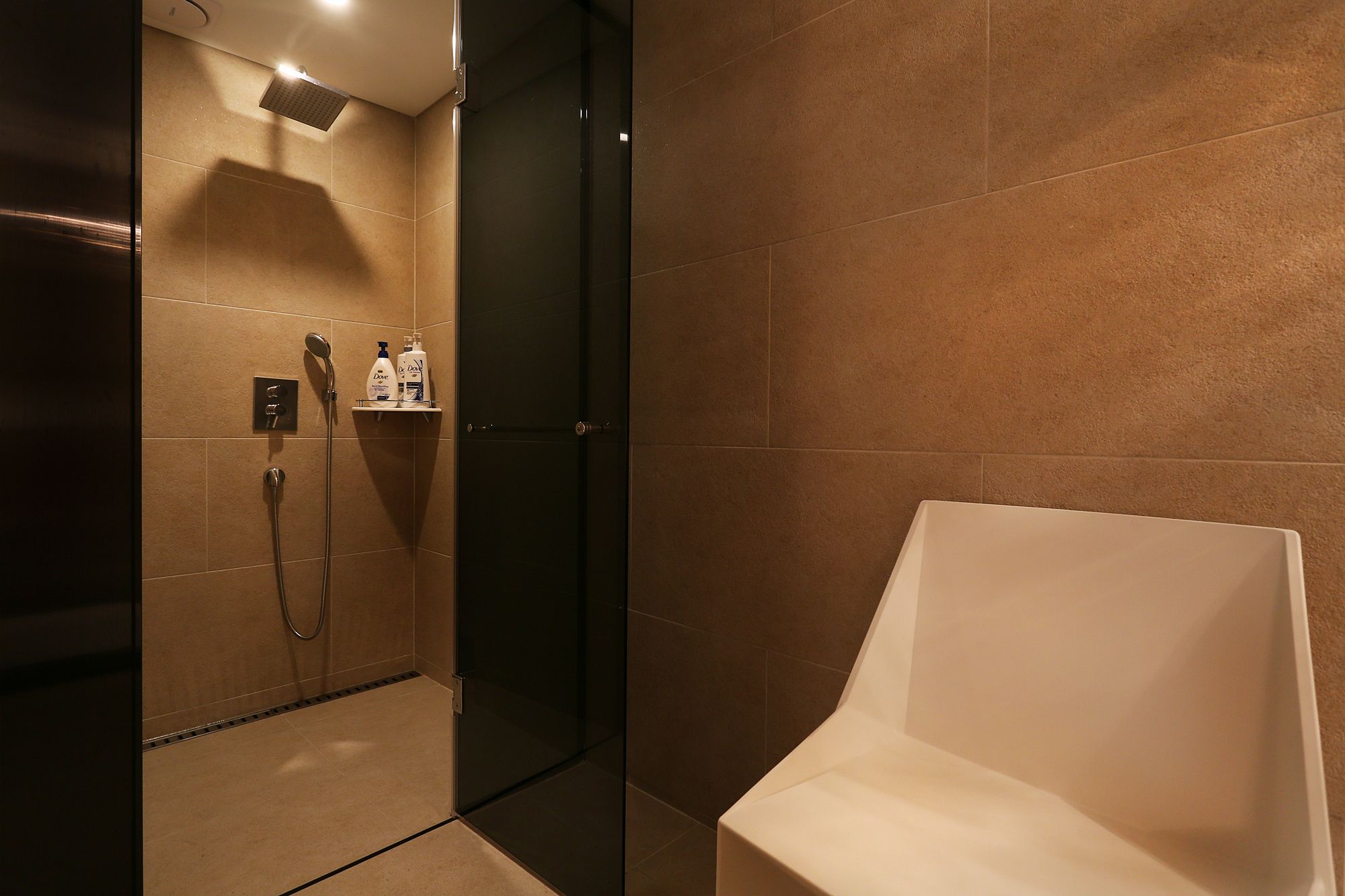 A modern bathroom with a shower, a glass door, and a white chair.