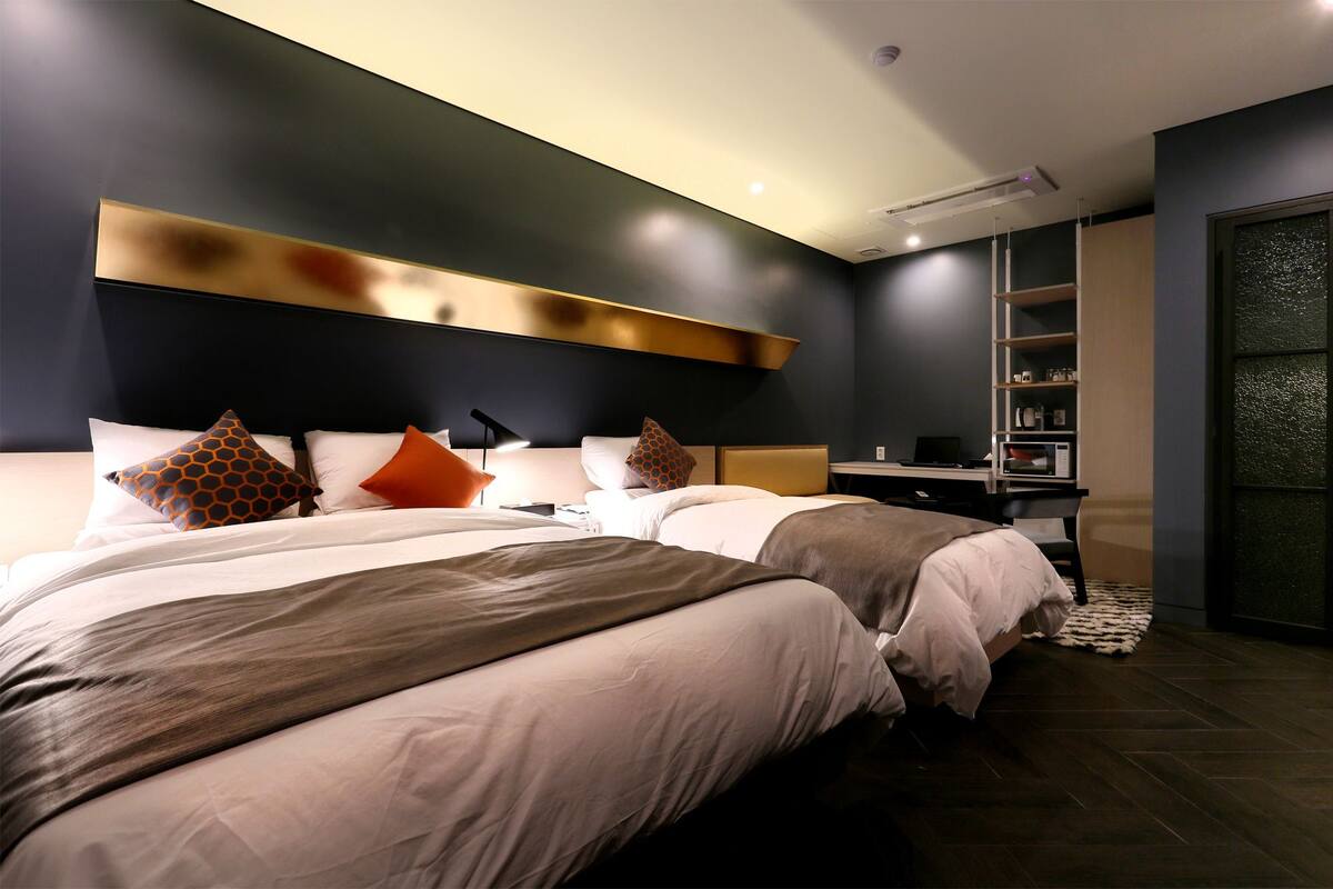 A modern hotel room with two beds, a desk, and a built-in wardrobe.