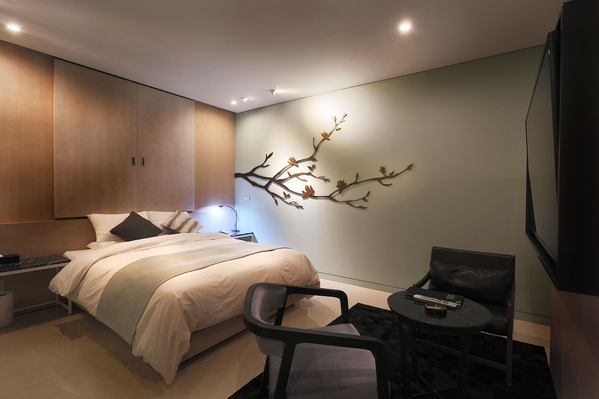 A modern hotel room with a bed, a desk, a chair, and a wall-mounted TV.