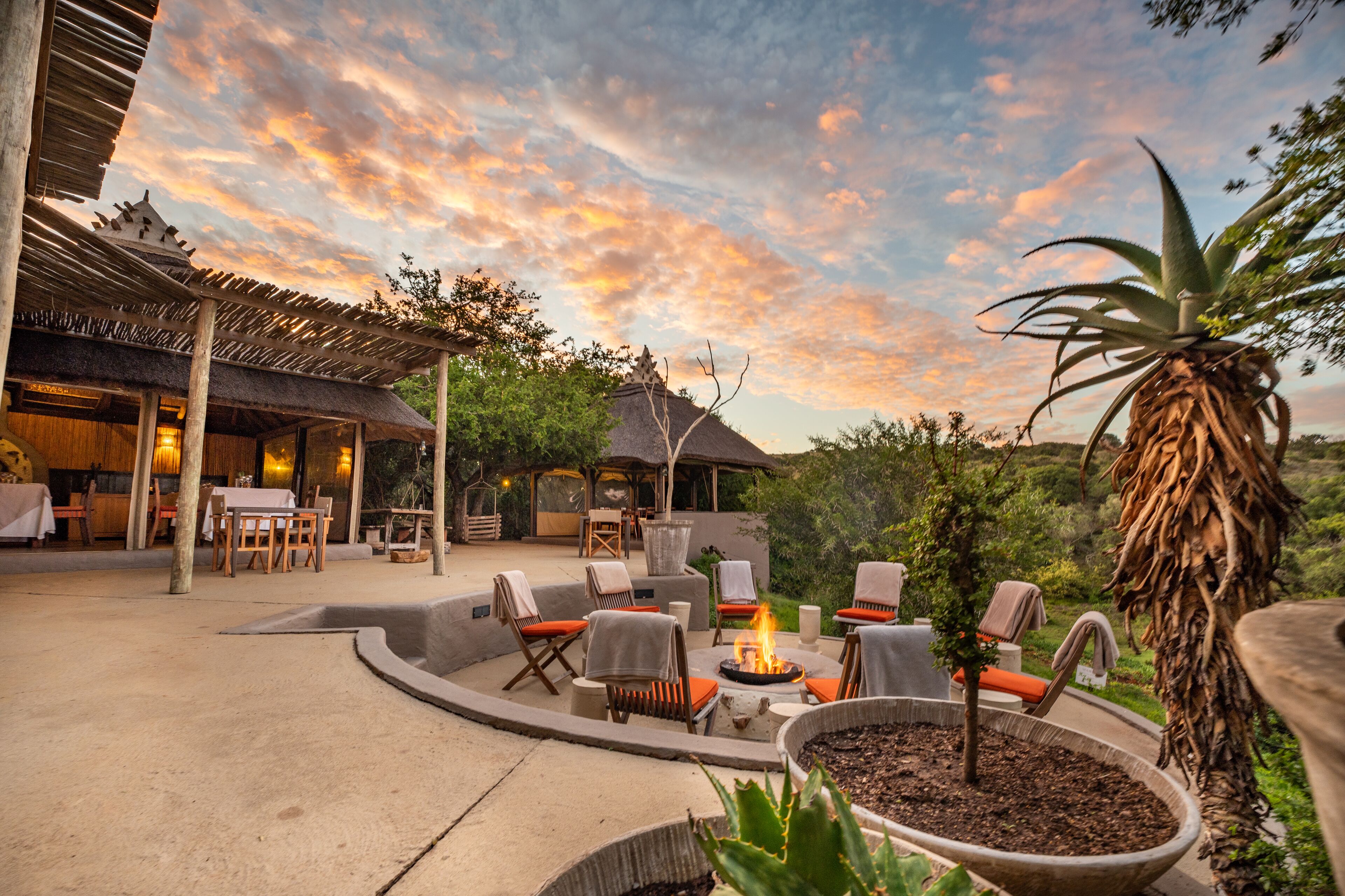 Un patio al aire libre con asientos, una chimenea y una estructura con techo de paja.