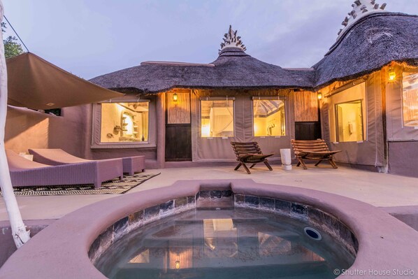 A spa area with a hot tub, lounge chairs, and a building with a thatched roof.