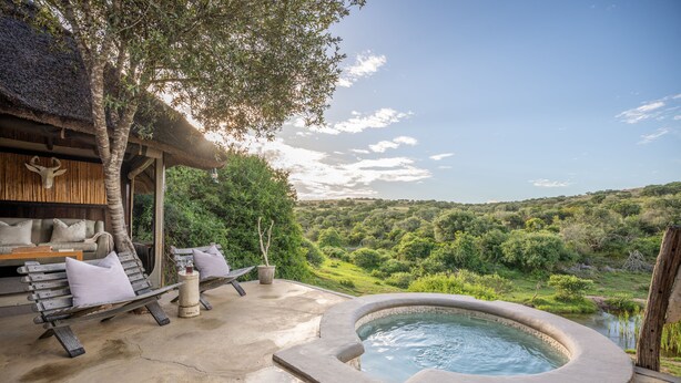 Un jacuzzi con revestimiento de piedra, un banco de madera con cojines y vistas a un paisaje exuberante.