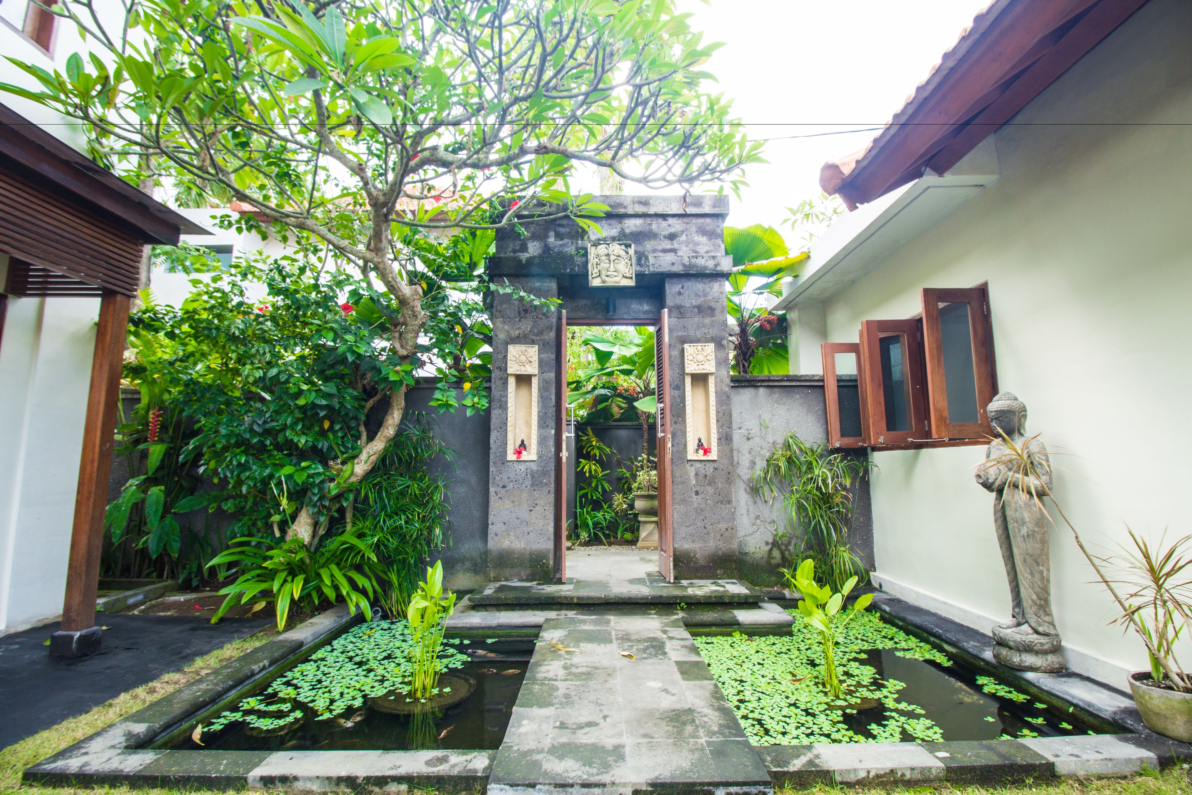 A traditional courtyard with a stone gateway, potted plants, and a small water feature.