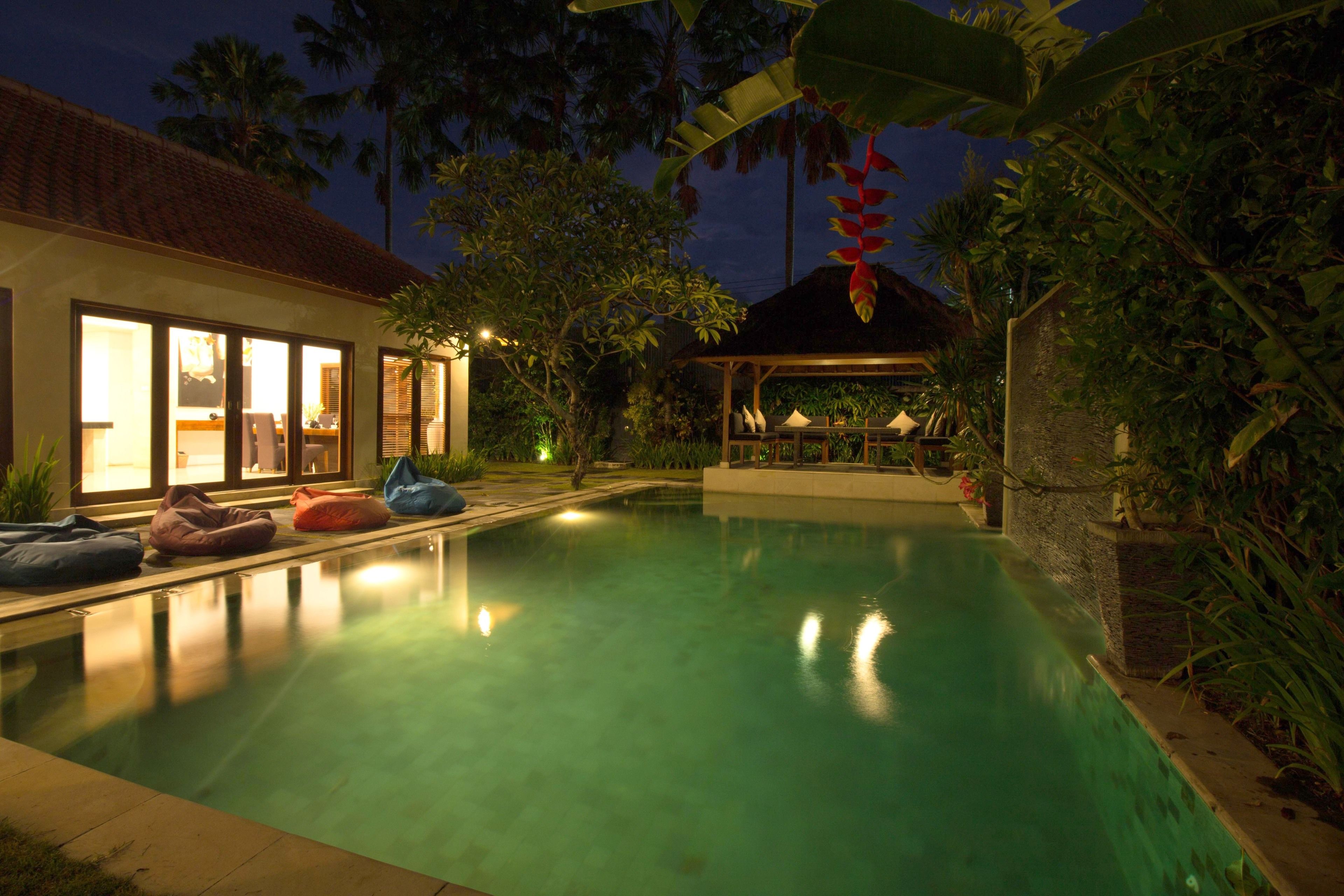 A swimming pool with bean bags, a covered seating area, and a house with large windows.