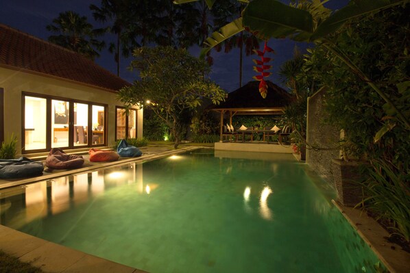 A swimming pool with bean bags, a covered seating area, and a house with large windows. - Amore Villas (Canggu)