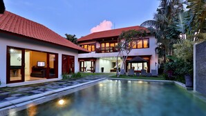 Una casa de dos pisos con piscina, ventanas amplias y un balcón.