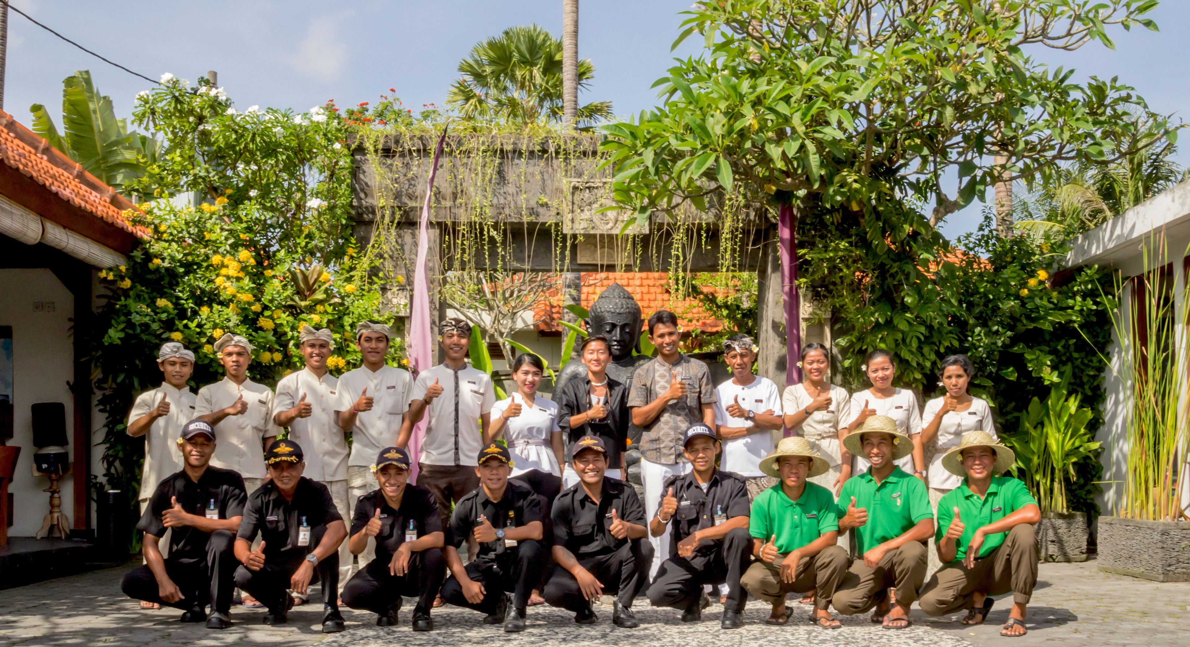 Un groupe de personnes posant dans un cadre extérieur, avec un mélange de verdure et d’éléments architecturaux.
