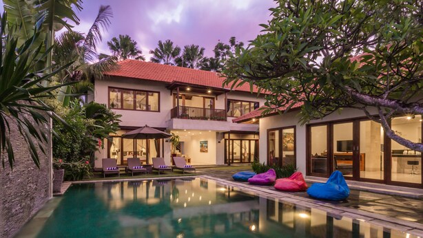 Una casa de dos pisos con piscina, mobiliario exterior y balcón.