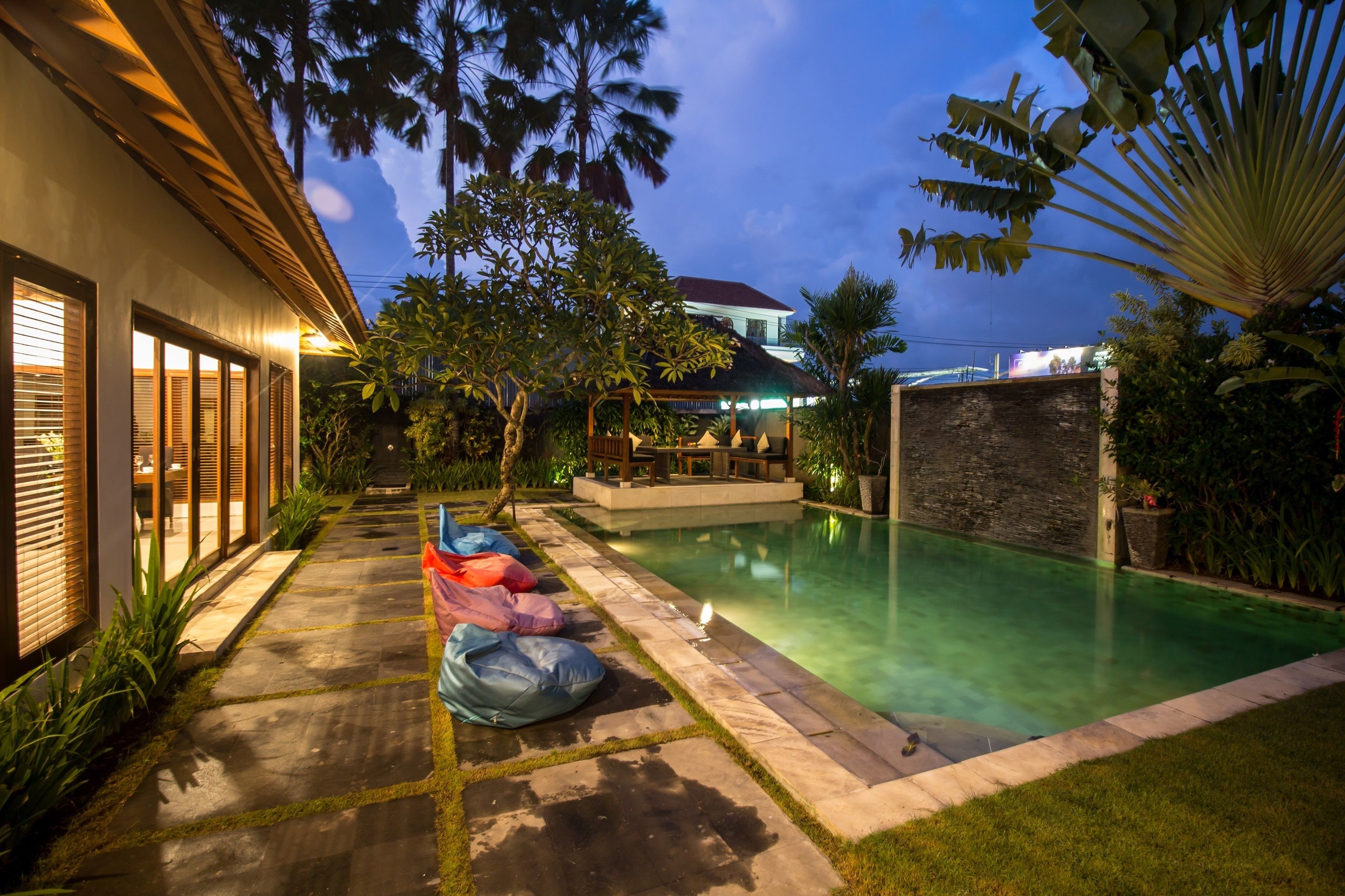 A nighttime pool area with a stone pathway, seating, and lush greenery.