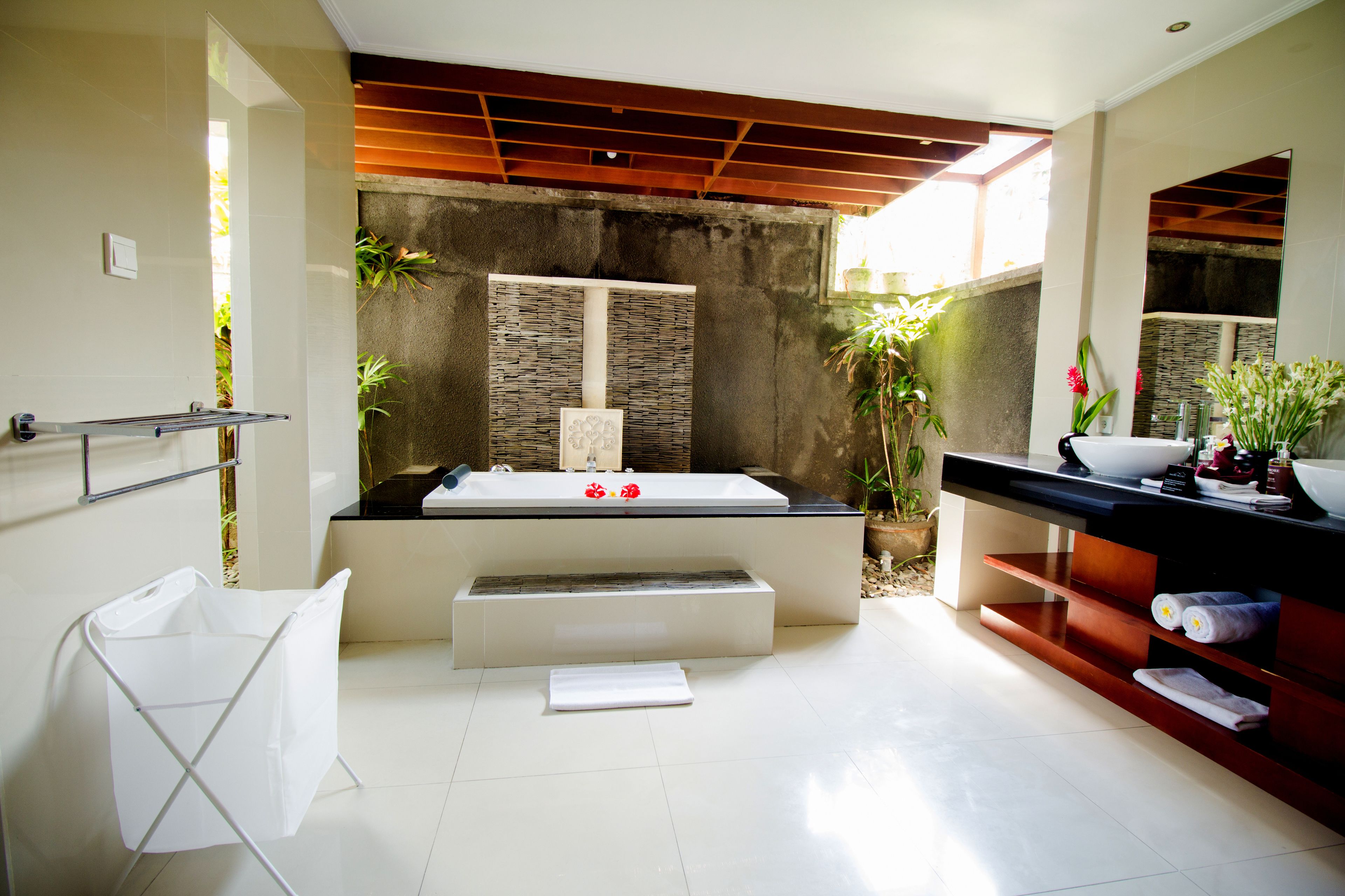 A modern bathroom with a large bathtub, a wooden ceiling, and a stone wall.