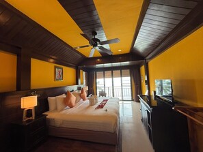 A hotel room with a large bed, a ceiling fan, a television, and a balcony with a view. - Baan Krating Khao Lak Resort (Takua Pa)