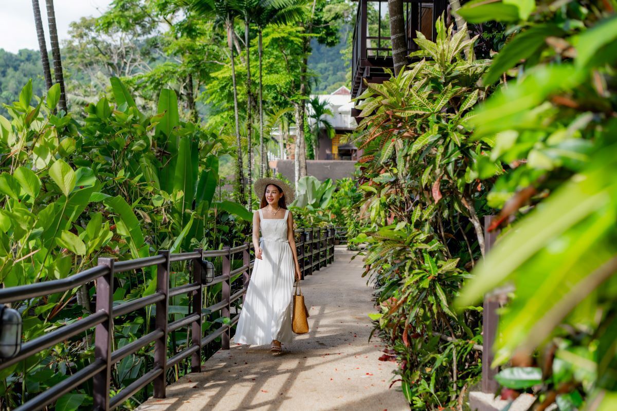 A woman in a white dress walking on a bridge surrounded by lush greenery.