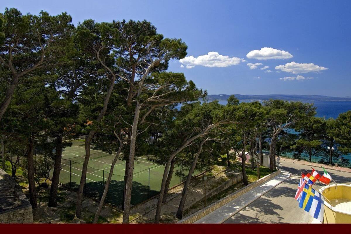 A tennis court surrounded by trees, with a clear view of the sea and distant land.