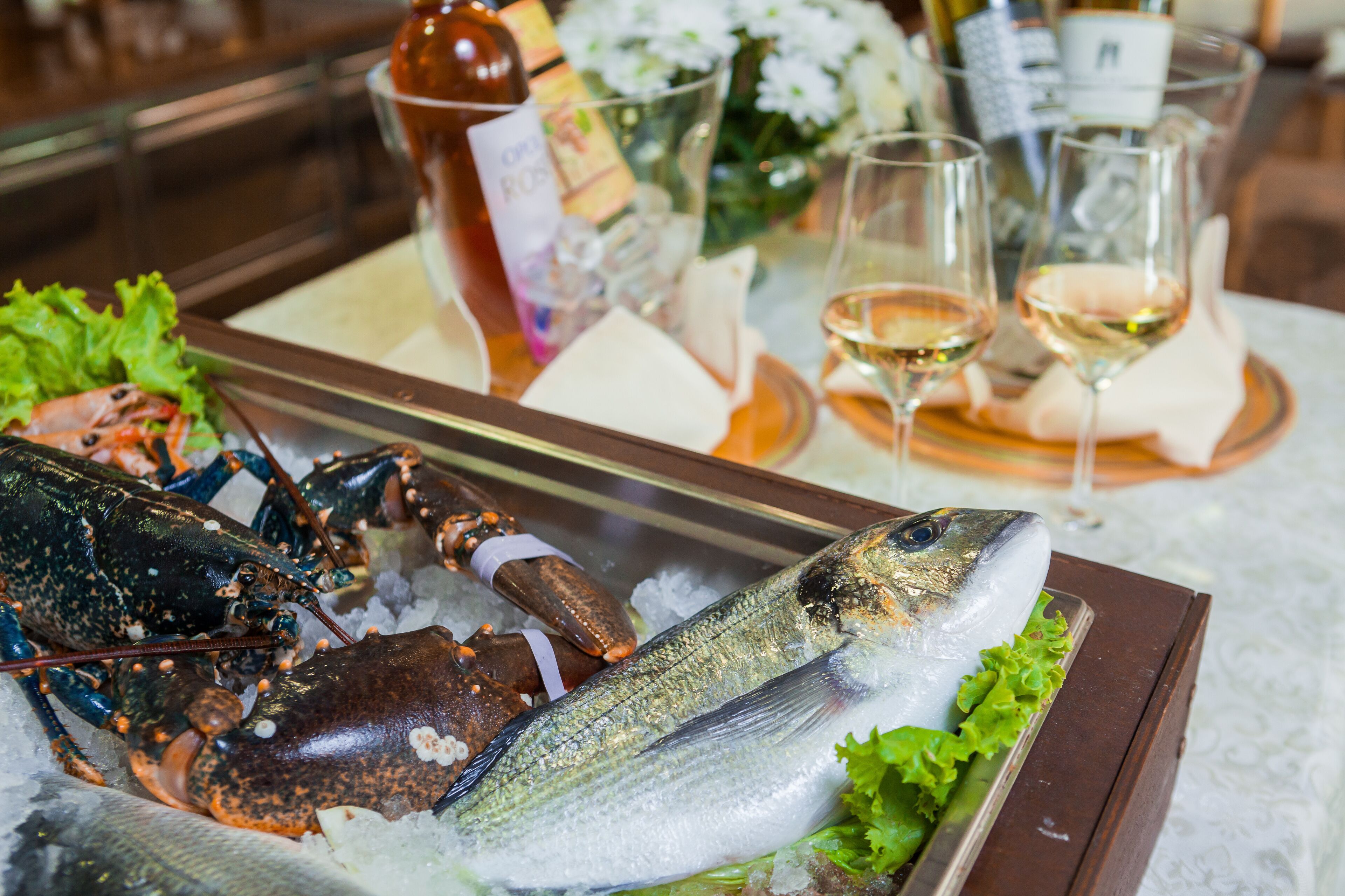 A seafood platter with lobster and fish on ice, accompanied by glasses of white wine and a bottle of rosé wine.