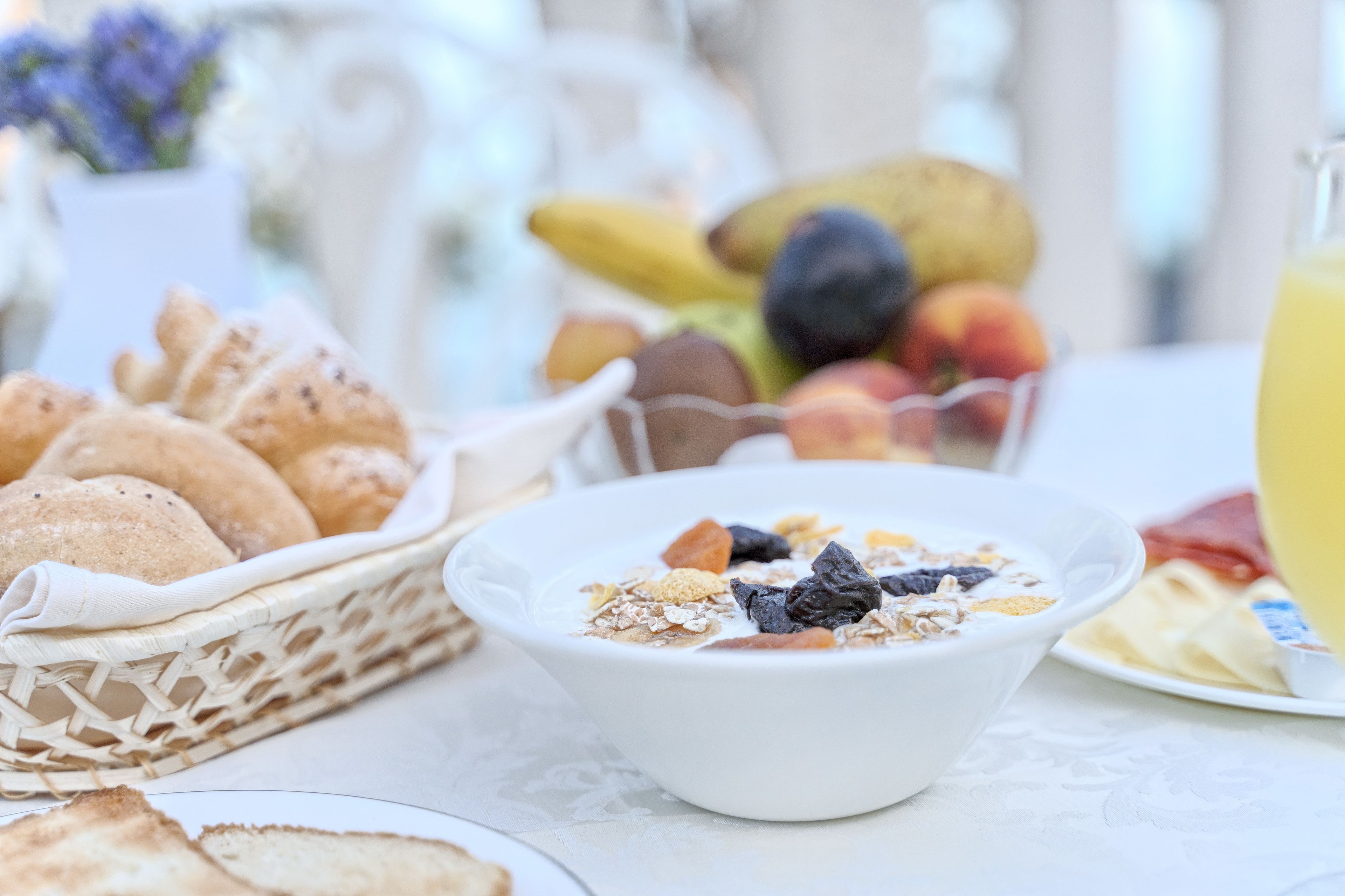 A breakfast setting with a bowl of cereal, a basket of bread, and a plate of fruits.