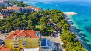 An aerial view of a coastal hotel with multiple buildings, a beach, and clear blue waters. - Hotel Bacchus (Baska Voda)