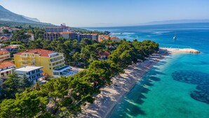 An aerial view of a coastal area with buildings, a beach, and clear blue waters. - Hotel Bacchus (Baska Voda)