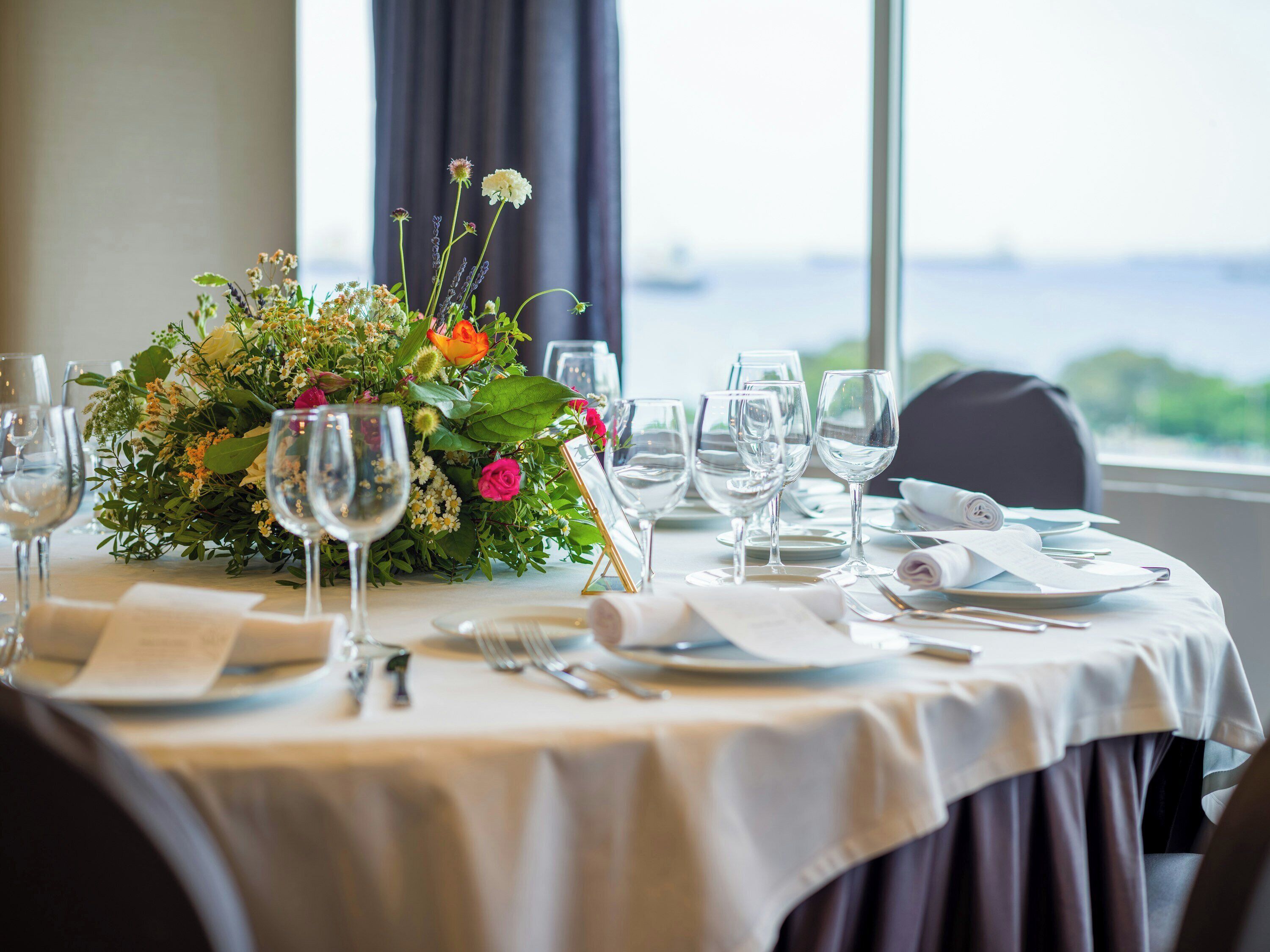 A table set for dining with a floral centerpiece, clear glassware, and a view of the outdoors.