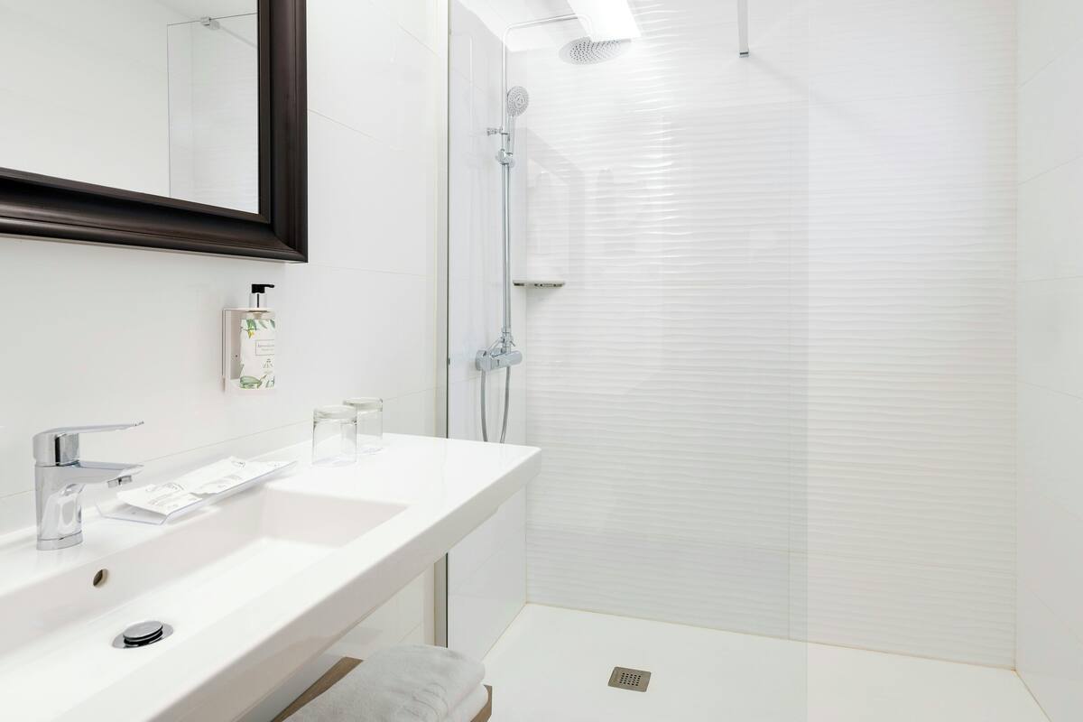 Un baño moderno con lavamanos blanco, espejo y cabina de ducha de vidrio.