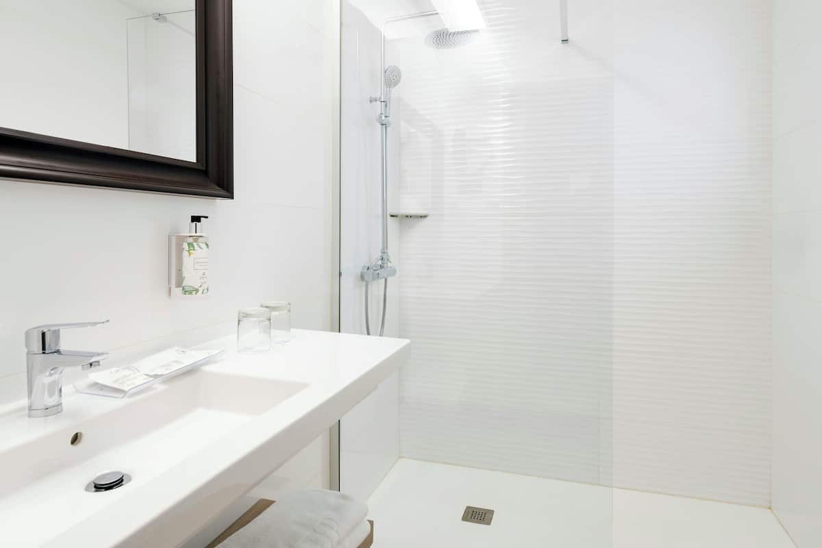 Une salle de bain moderne avec un lavabo blanc, un miroir et une douche en verre.