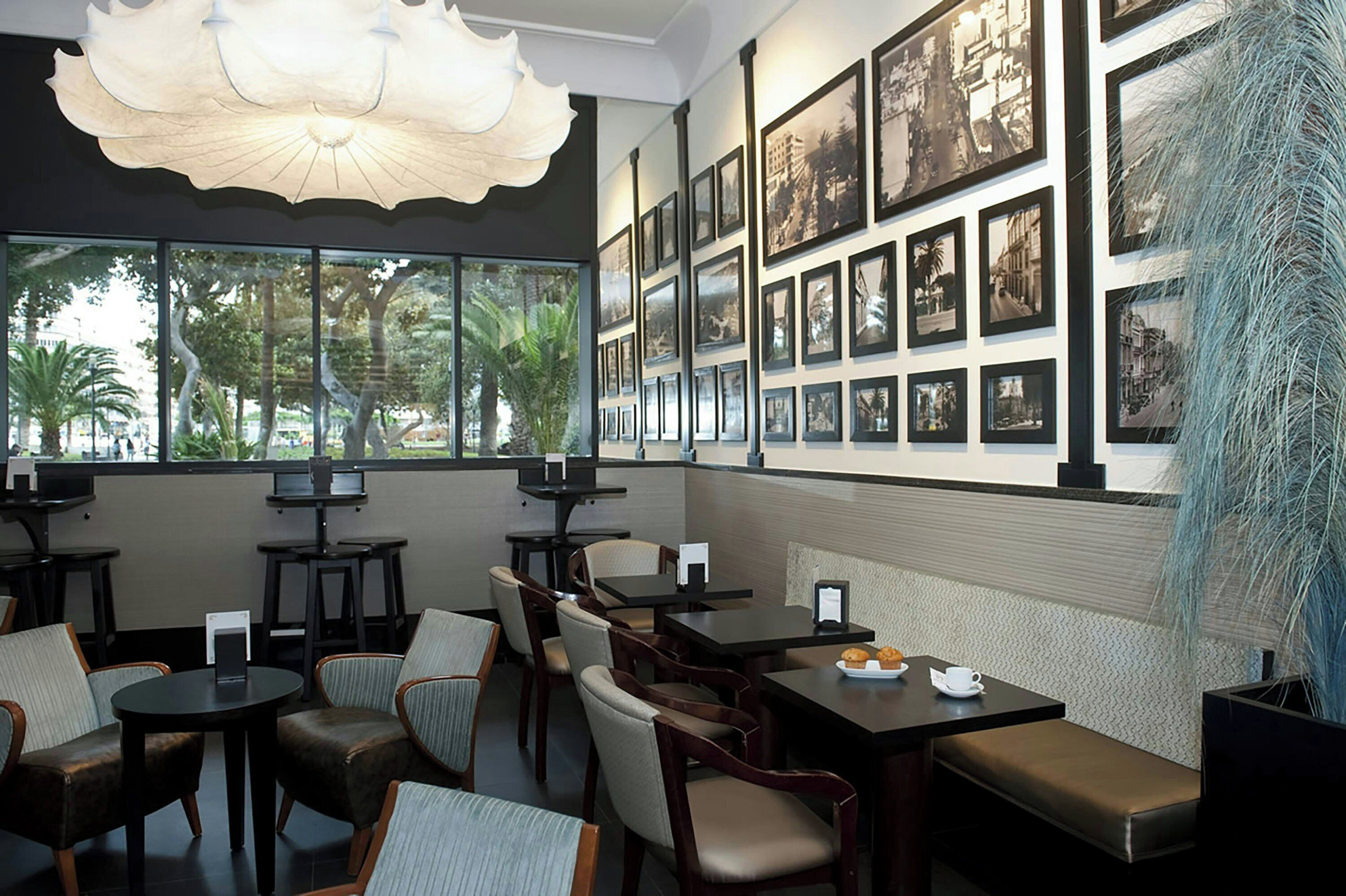 Un restaurant avec des tables et des chaises, des tableaux encadrés aux murs et une vue sur les palmiers à l’extérieur.