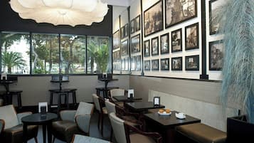 Un restaurant avec des tables et des chaises, des tableaux encadrés aux murs et une vue sur les palmiers à l’extérieur.