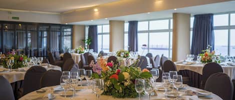 A dining area with round tables, each set with plates, cutlery, and wine glasses, and floral centerpieces.