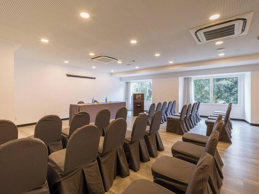 Ein Konferenzraum mit einem langen Tisch, Stühlen, einem Rednerpult und großen Fenstern.