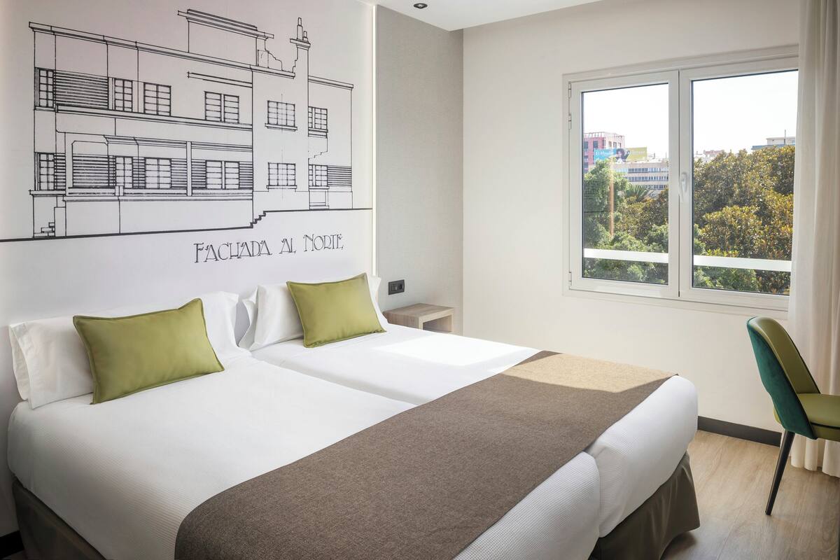 Una habitación de hotel con dos camas, un ventanal grande y un dibujo arquitectónico colgado en la pared.