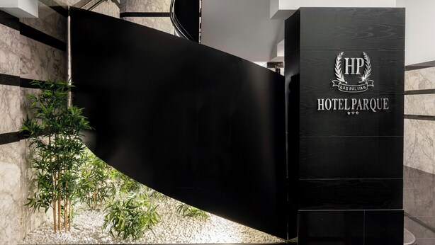 Een moderne hotel receptie met een zwart receptiebalie, een marmeren wand en een kleine binnentuin.