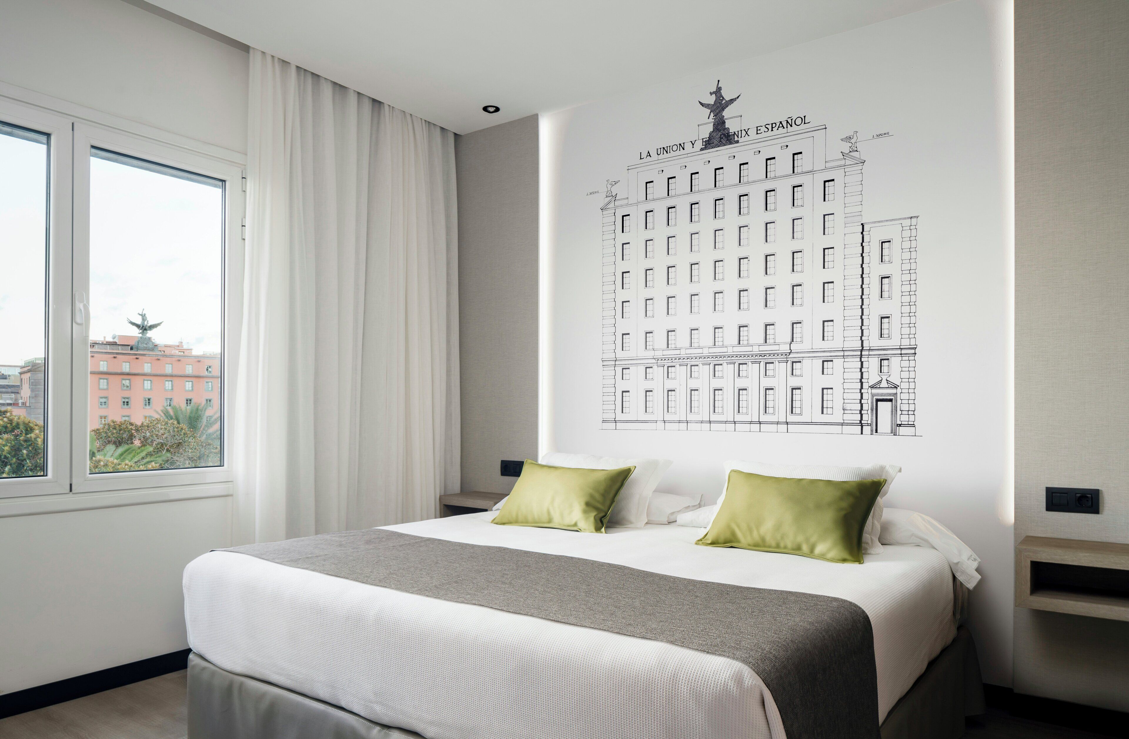 Habitación de hotel con una cama grande, una ventana con cortinas, un mural en la pared y vistas a edificios.