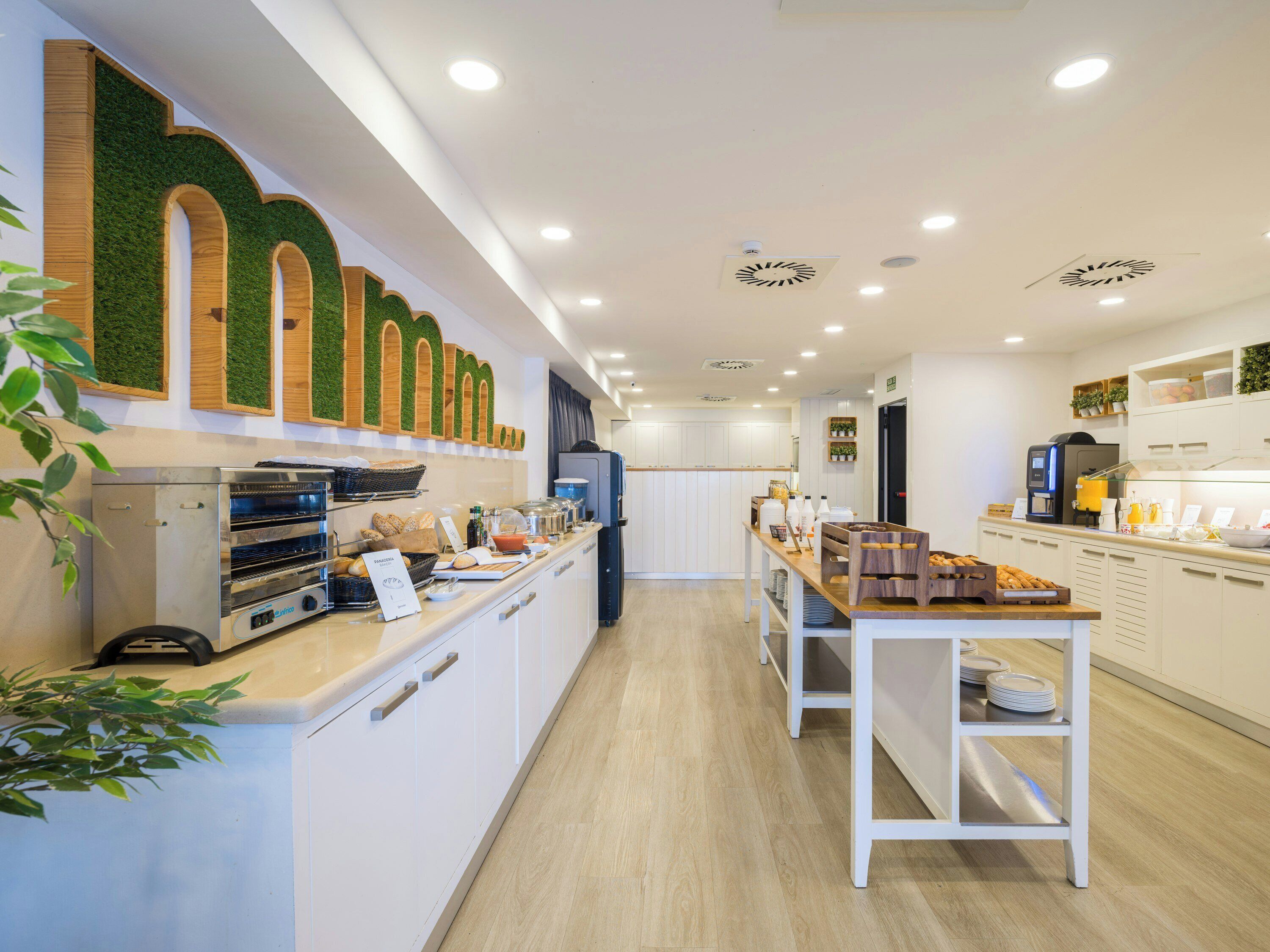 A modern cafe with a long counter, a coffee machine, and a display of bread and pastries.