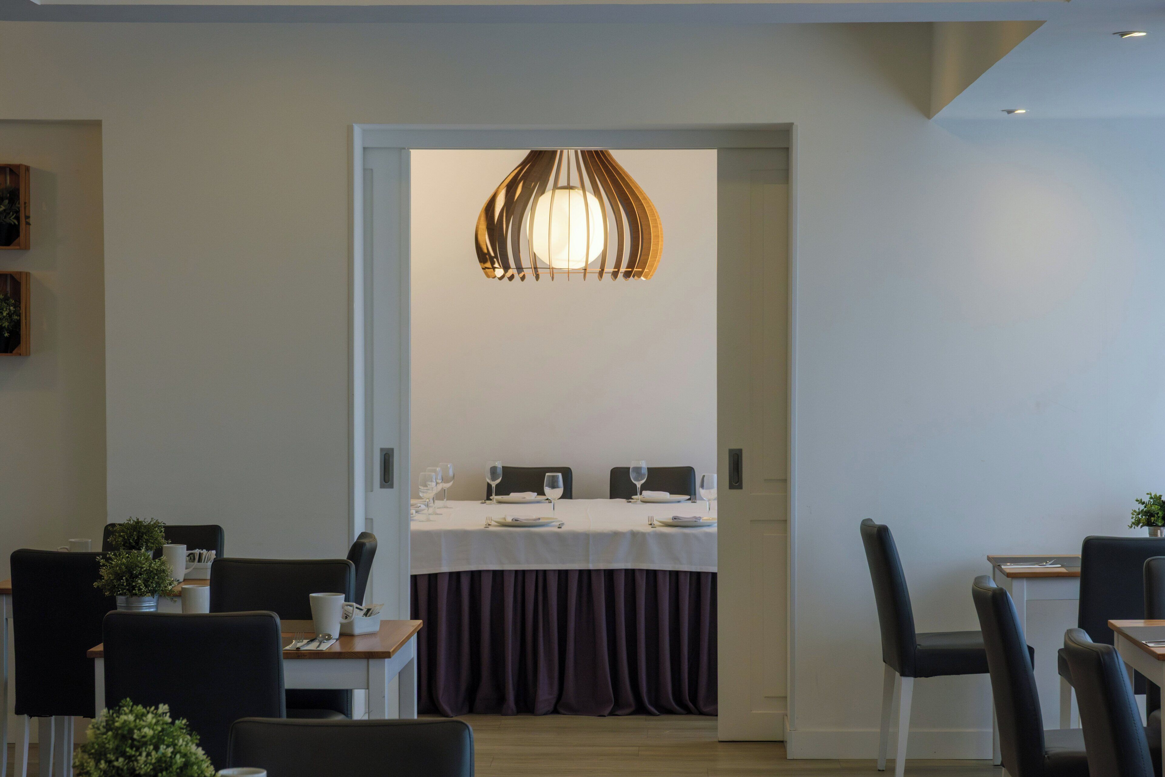 A modern dining area with a table set for two, a decorative hanging light, and black chairs.