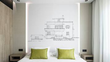 Un dormitorio con una cama, dos almohadas verdes, un cabecero blanco y un dibujo arquitectónico colgado en la pared.