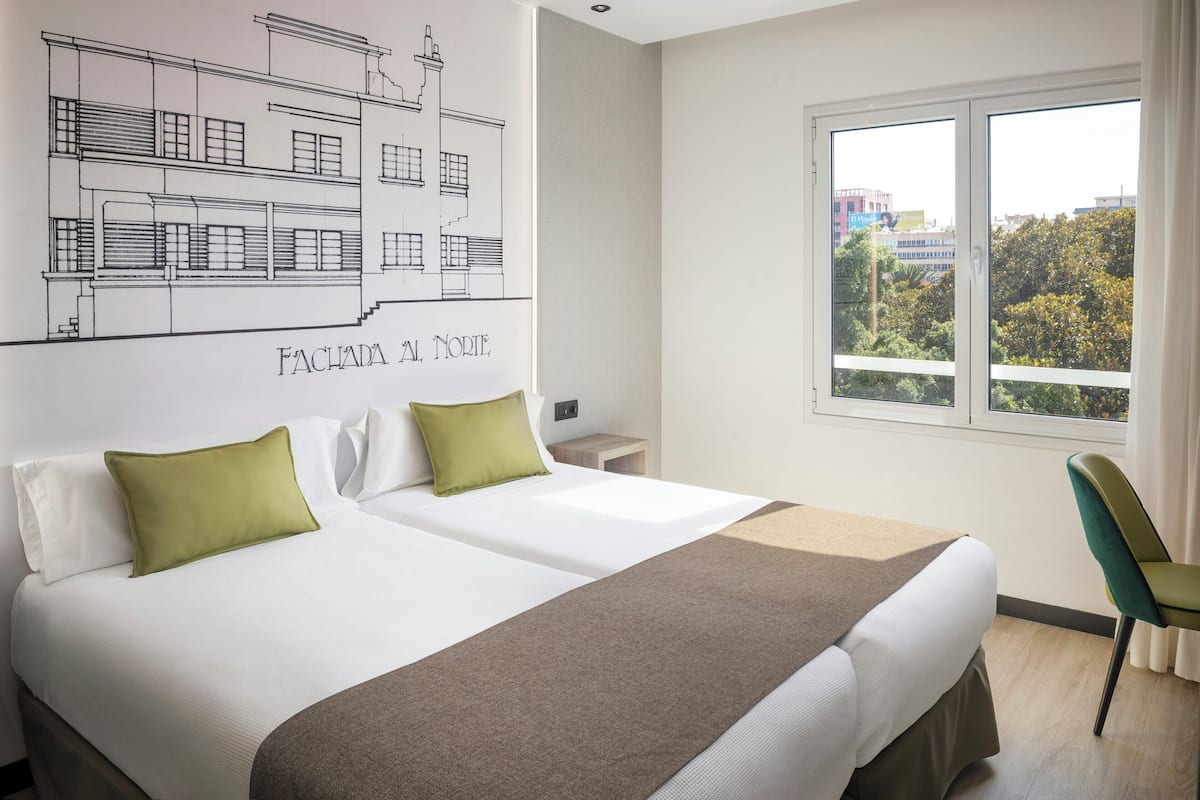 Une chambre dâhĂŽtel avec deux lits, une grande fenĂȘtre et un plan architectural accrochĂ© au mur.