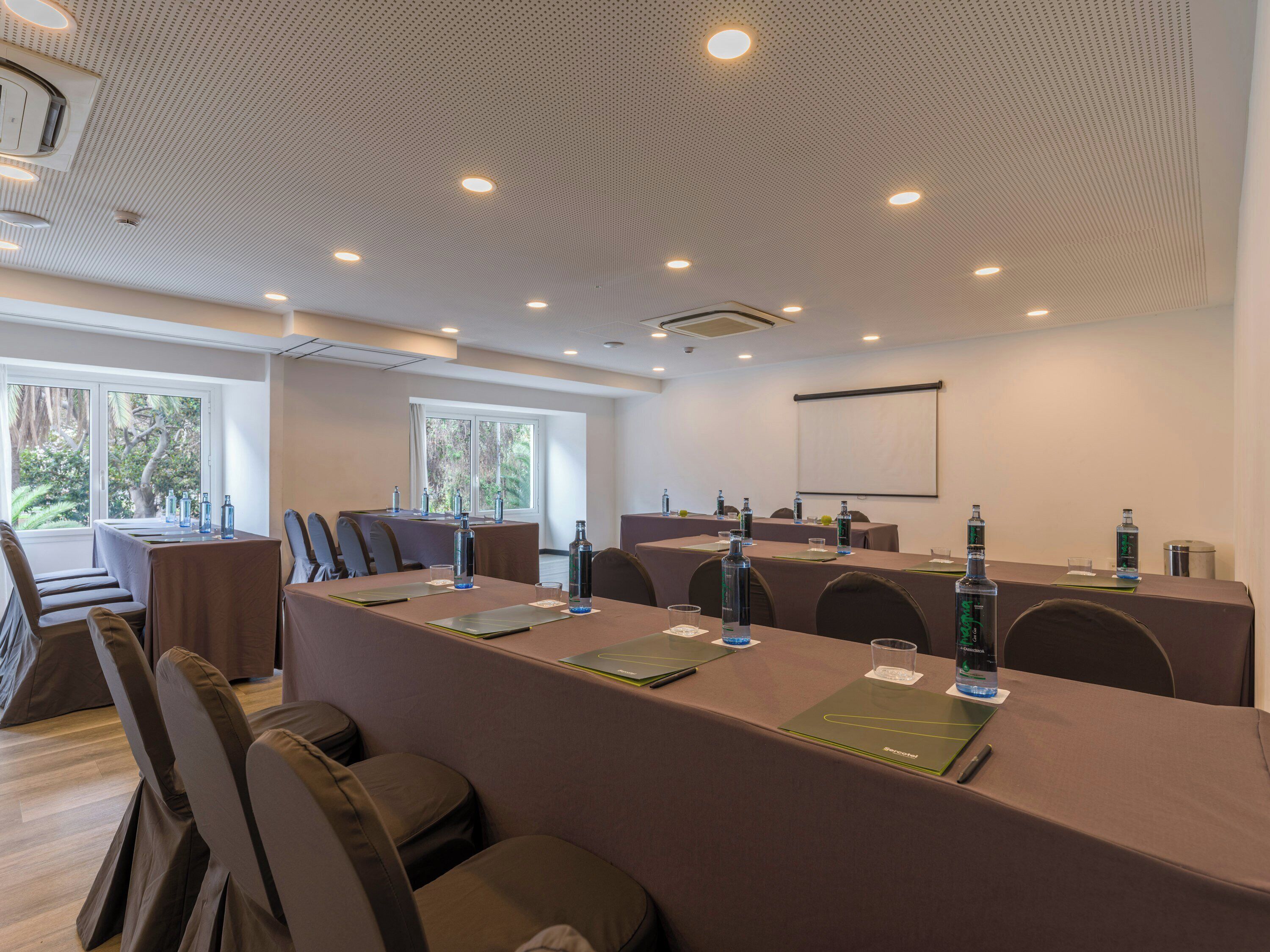 A conference room with a long table, chairs, a projector screen, and a large window.