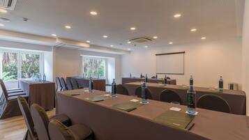 A conference room with a long table, chairs, a projector screen, and a large window.