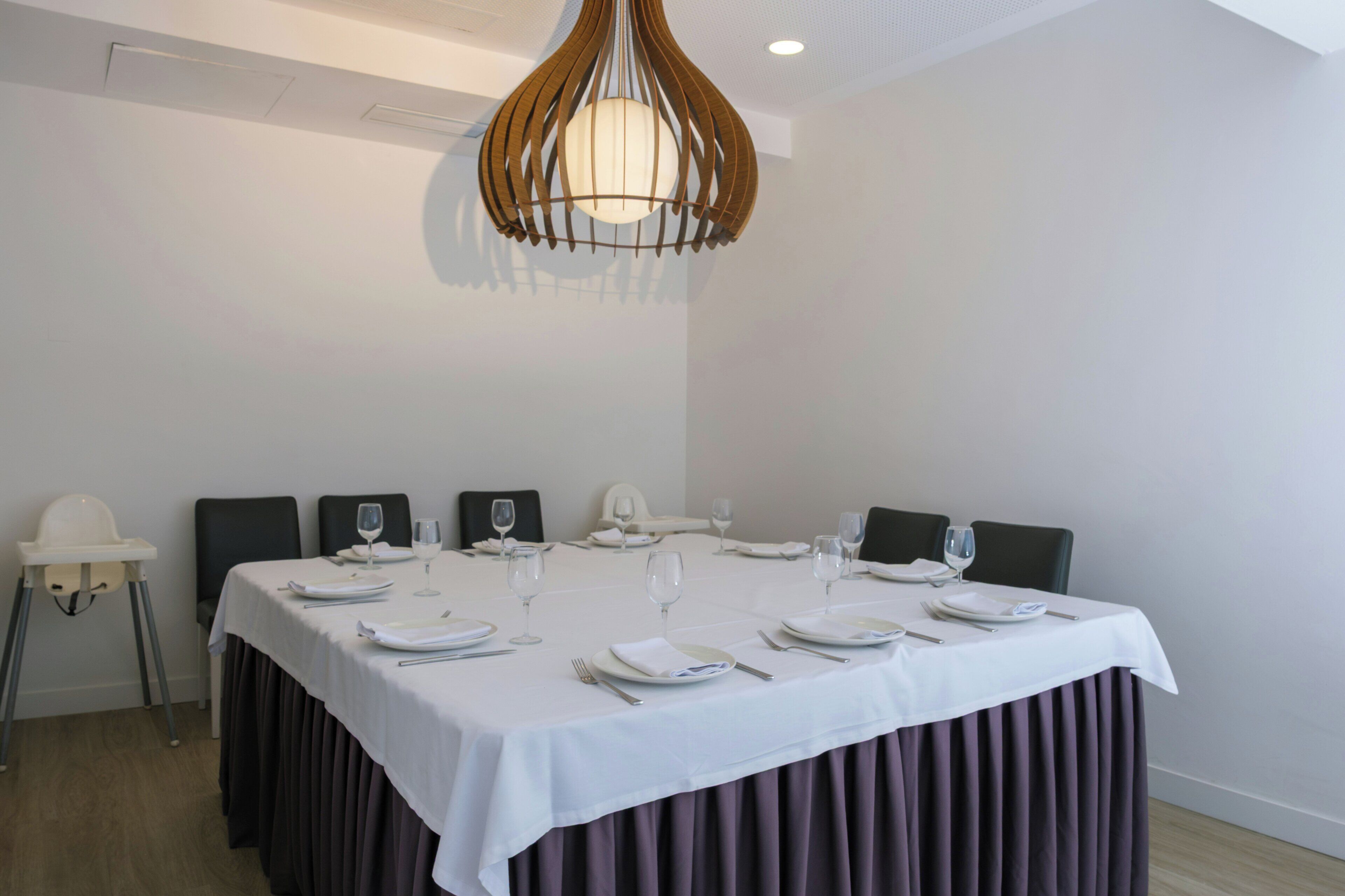 Un salón de conferencias con una larga mesa dispuesta para una reunión, equipado con sillas, platos, vasos y una lámpara colgante original.