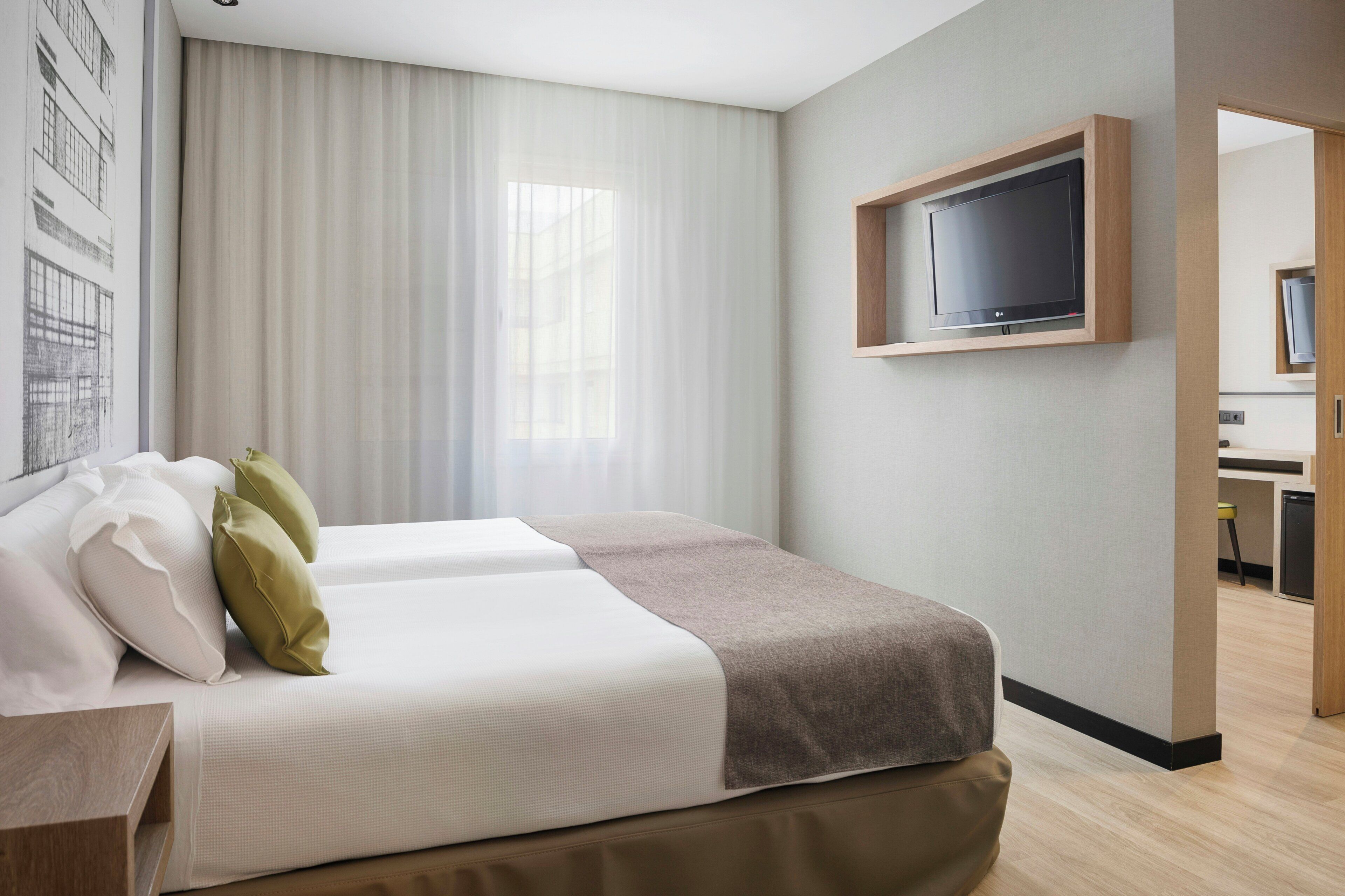 A hotel room with a bed, a television mounted on the wall, and a view of the outside.
