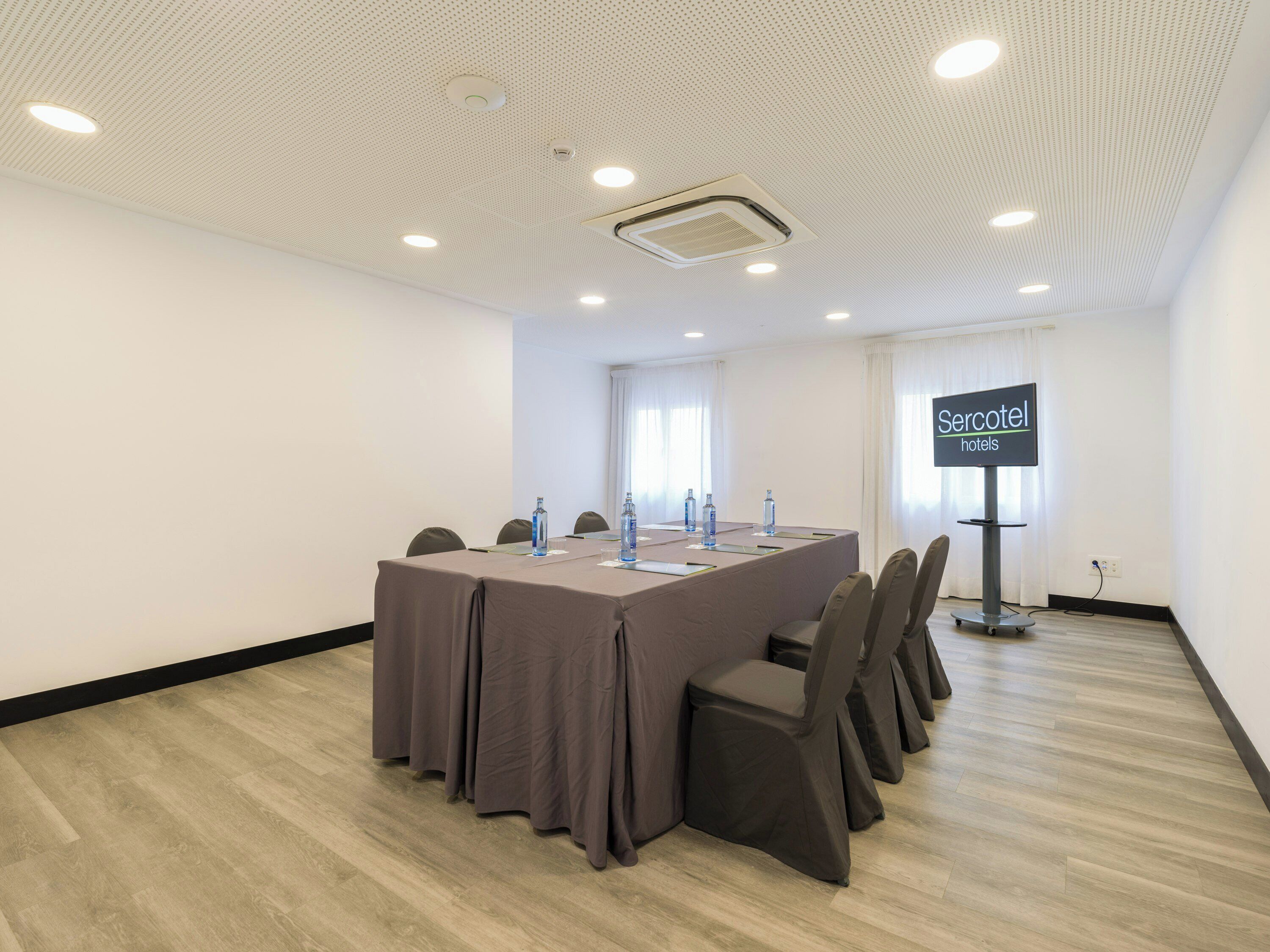 Un salón de conferencias con una larga mesa, sillas, una pantalla de proyector e iluminación empotrada en el techo.